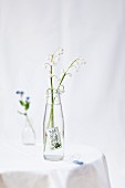 Maiglöckchen in kleiner Limoflasche als Vase mit Vergissmeinnicht-Briefmarke verziert