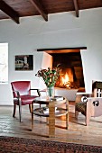 Chair, armchair and round table in front of open fire in rustic, eclectic interior