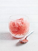 Watermelon granita in a glass with a spoon on a white-painted wooden surface
