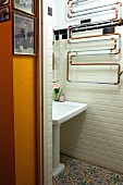 Artistic arrangement of heating pipes above vintage-style sink on tiled wall