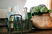 Flaschenträger aus Metall mit Glasflaschen, daneben Hortensien in Keramikvase