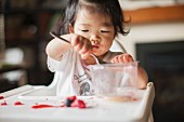Asiatisches Kleinkind isst Früchte im Hochstuhl