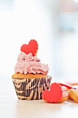 A cupcake topped with pink buttercream and a heart-shaped biscuit