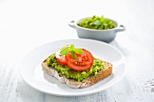 A slice of bread topped with a pea spread and tomatoes