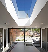 Esszimmer mit Oberlicht in Decke über Küchentheke, helle Arbeitsplatte, im Hintergrund Schiebetüren vor sonnigen Terrasse mit verschiedenen Ebenen