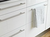 White kitchen base cabinets with stainless steel strip handles and polka-dot tea towel hanging over one handle