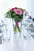 Bouquet of pink flowers, wine glasses and water glasses on festively set table