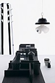 Schwarze Gefässe auf Filztabletts auf einem Tisch, Lampenskulptur und Garderobenständer im Hintergrund