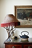 Antlers arranged around table lamp and Oriental teapot on antique cabinet; Buddha figurine and oil painting in background