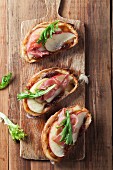 Crostini topped with apple sauce, apple slices and ham on an old chopping board