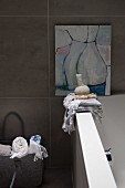 Towels on edge of bathtub below modern artwork on tiled wall