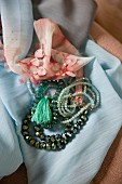 Verschiedene Halsketten mit Perlen auf pastellblauem Tuch und nostalgischem Flair