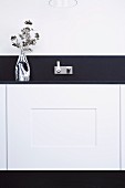 Vase of flowers on dark worksurface in designer kitchen with modern, angular, wall-mounted tap fitting