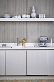 Kitchen counter and floating shelf on exposed concrete wall in minimalist, white, designer kitchen