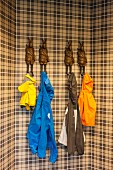 Colourful raincoats hanging on coat pegs in shape of anthropomorphic hares on brown tartan wall