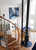 View from mezzanine down spiral staircase into double-height interior with central stovepipe and photo poster of sailing yacht