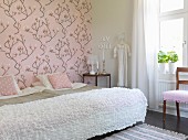 Twin beds pushed together with white blanket in romantic bedroom with pink, magnolia-patterned wallpaper
