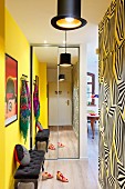 Mirrored wardrobe and antique upholstered bench in hallway with one yellow wall and wallpaper with graphic pattern