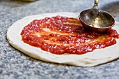 Tomato sauce being spread on a pizza base