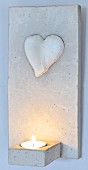 An Wand gehängtes Windlicht aus Beton mit appliziertem Herz und brennende Kerze