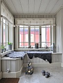 Grey sheepskin blankets on window seat in wood-clad conservatory with fabric roller blinds on lattice windows