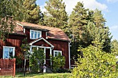 Rotbraun gestrichenes Holzhaus in sommerlichem Garten