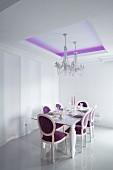 Elegant gedeckter Esstisch und Kristallkronleuchter in Esszimmer mit violetter indirekter Deckenbeleuchtung und neobarocken Polsterstühlen