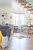 Sofa and dining area in open-plan interior in pastel shades with cat sitting on cantilever staircase