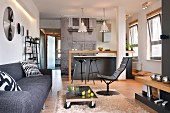 Lounge area with modern, grey couch and low table on castors on flokati rug in front of kitchen area in open-plan interior