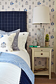 Bett mit blauem Kopfteil und Tapete im Landhausstil, Nachttisch mit Lampe
