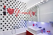 Schriftzug neben Herz und Lippenstift Motiv auf schwarz gepunkteter Badezimmerwand, Spiegelfront mit Leuchtenreihe über Waschbecken