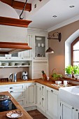 Kitchen counter with wooden worksurface and white, country-house-style base and wall units