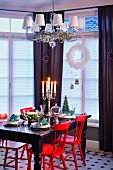 Red-painted chairs at black table below chandelier with small lampshades