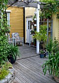 Blick vom Garten auf Veranda mit Holzboden, an gelber Holzfassade Armlehnstühle