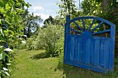 Blaues, offenes Vintage Holztor in sommerlichem Garten