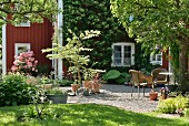 View from garden to furnished gravel terrace and Falu-red wooden house in summer atmosphere