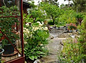 View from green house along stone path lined with flowerbeds to pond