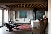 Loungebereich mit Klassiker Sessel und weiße, moderne Couchgarnitur in Loft-Wohnbereich mit rustikaler Holzbalkendecke