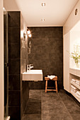 Designer bathroom with grey tiles on walls and floor, minimalist fittings and custom shelving below window in niche
