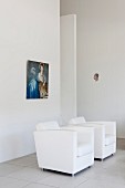 White, designer armchairs below picture on wall in minimalist interior