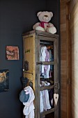 Girl's clothing hung in vintage cupboard and white teddy bear in corner of grey-painted room