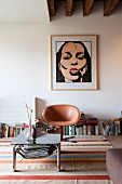 Coffee table with metal frame in front of pale brown, retro leather easy chair on brightly striped rug and modern portrait of woman on wall