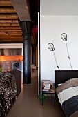 Offener Schlafbereich mit Designerwandleuchten, Blick auf schwarze Metallsäulen und Edelstahlküche in Loftwohnung