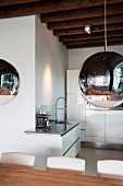 Spherical lamps with chrome and transparent surfaces in front of modern, white kitchen