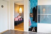 Vorraum mit halboffenem Garderobenschrank neben offener Tür und Blick ins Wohnzimmer auf Pendelleuchte