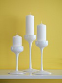 White candles in three-piece, white china candlestick set against yellow wall