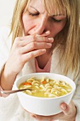 A woman with a cold eating chicken noodle soup
