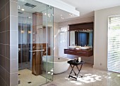 Rainfall shower and wooden column with row of shower nozzles in luxury shower in front of free-standing bathtub and exotic wood washstand
