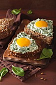 A sunflower seed roll topped with spinach cream cheese and fried eggs