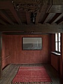 Teppichläufer auf Holzdielenboden, Bild auf rotbrauner Wand in reduziert rustikalem Ambiente
